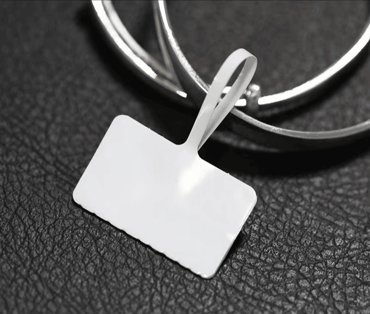 Празен бял RFID етикет за бижута е показан до гривни върху тъмна текстурирана повърхност за детайлно продуктово показване.