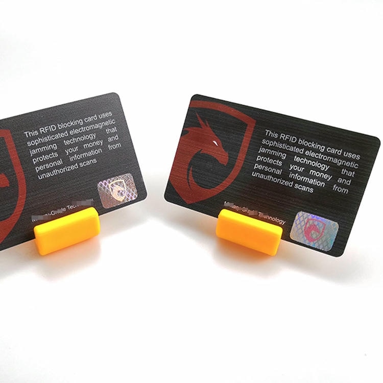Две RFID блокиращи карти с дизайн на червен дракон и щит стоят на жълти поставки показващи отпечатано защитно послание и холограмен елемент.