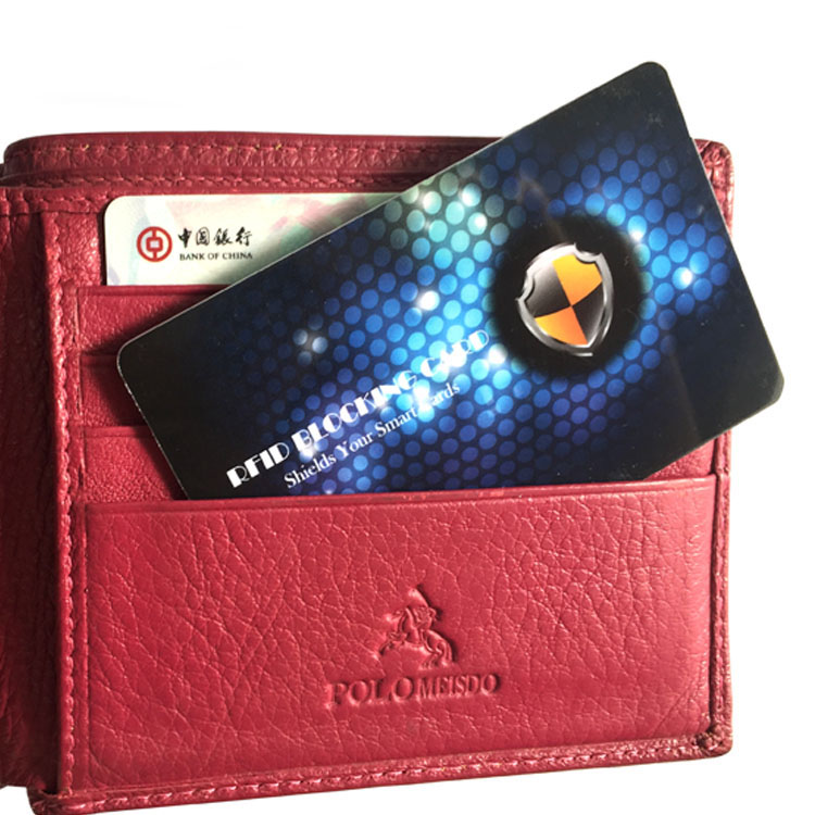 RFID блокираща карта, поставена в отделение на червен кожен портфейл пред банкова карта за ограничаване на риска от безжично сканиране.
