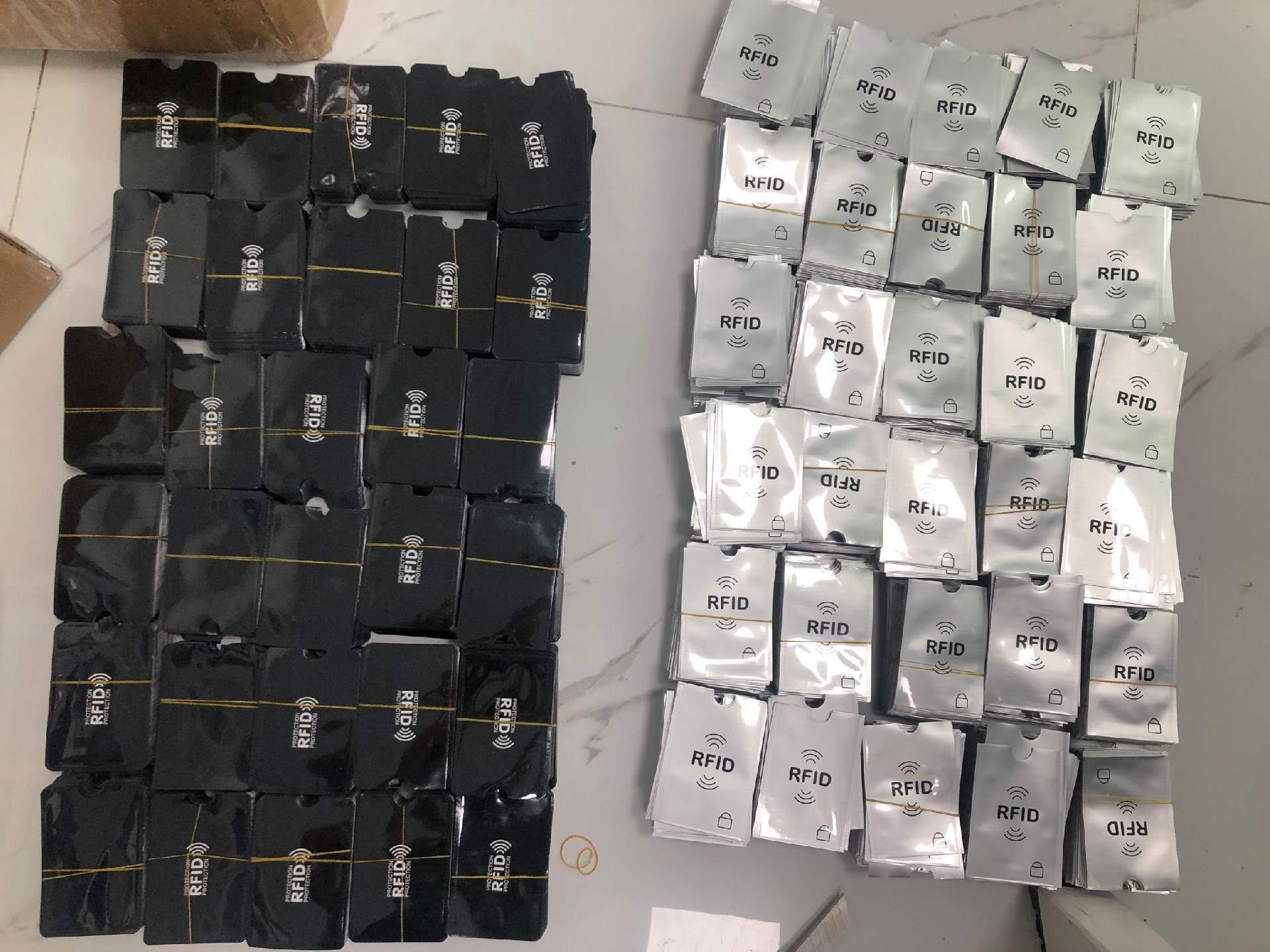 Купчини черни и сребристи RFID блокиращи калъфи са пакетирани с ластици и показват производствен капацитет за големи количества.