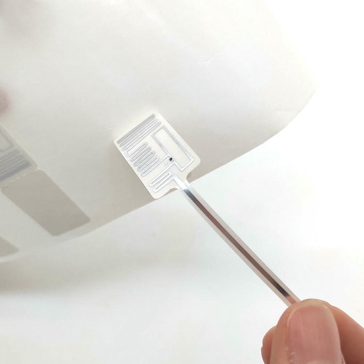Близък изглед показва единичен RFID етикет за бижута отделен от подложката за да разкрие модела на антената и структурата на етикета.