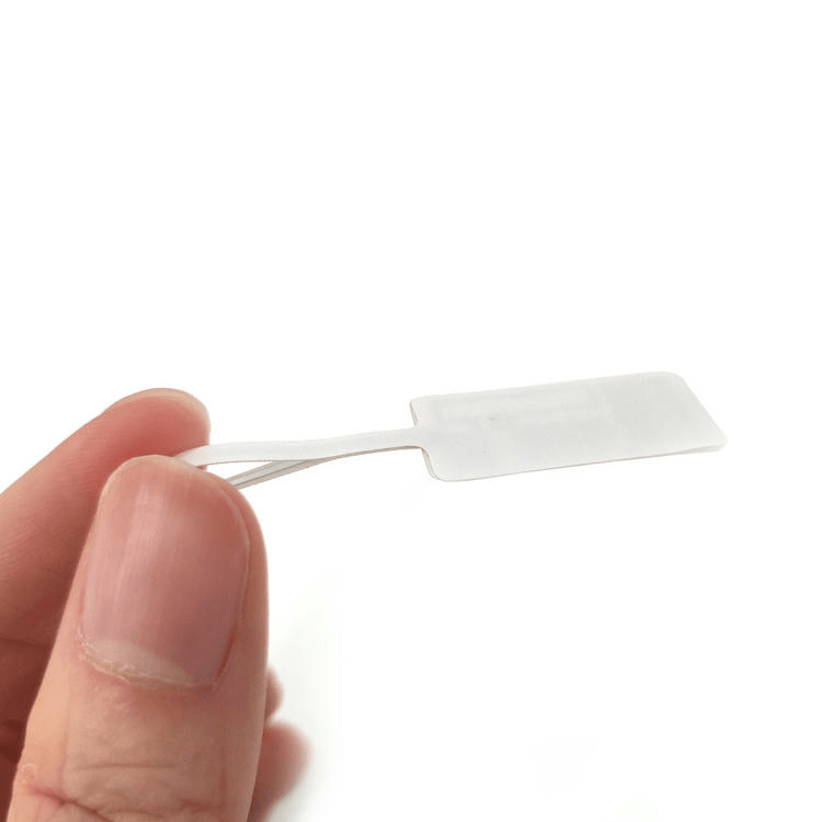 Ръка държи празната задна страна на RFID етикет за бижута, за да покаже гладката повърхност за печат и опашката за закрепване.