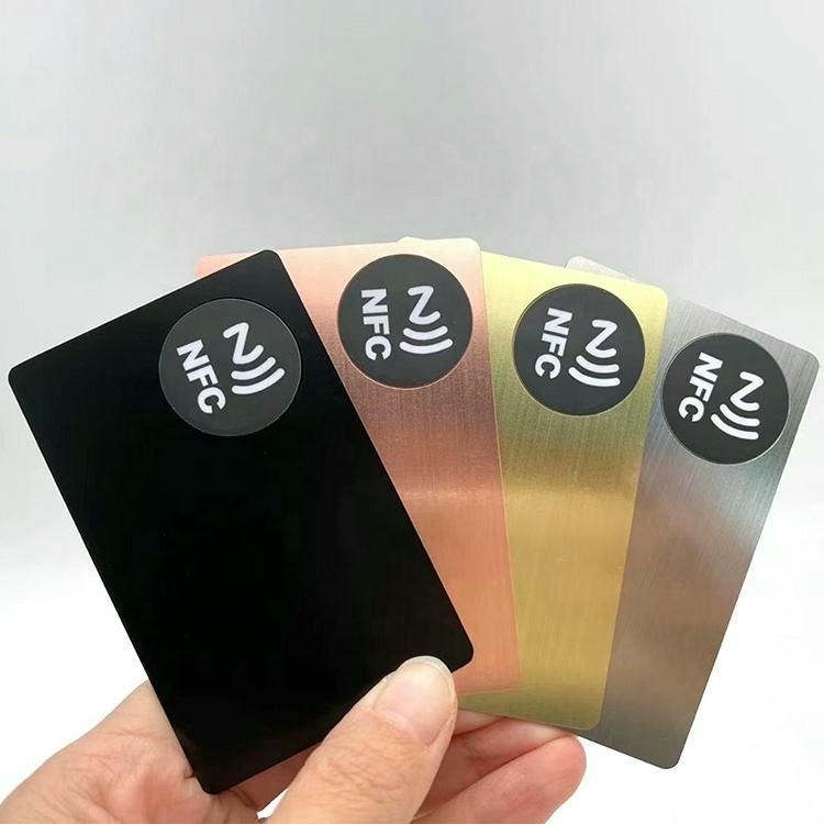Четири персонализирани метални визитки с NFC символи показващи черно розово злато златисто и сребристо покритие за сравнение на повърхностите.