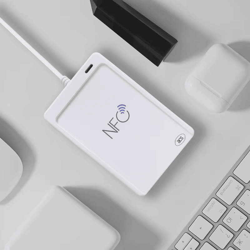 ACR1552U USB NFC четецът е разположен на работен плот сред компютърни аксесоари като пример за модерна работна среда.